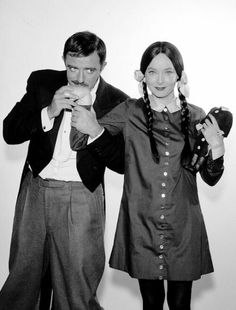 a man and woman standing next to each other in front of a white wall holding hats