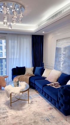 a living room with blue couches and chandelier hanging from the ceiling in front of a large window