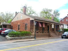 a small brick house with an american flag on it's porch and two cars parked in front