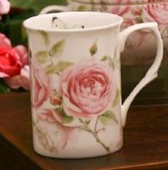 two coffee mugs sitting on top of a wooden table next to pink and red flowers