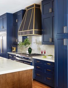 a kitchen with blue cabinets and white counter tops, gold trimming on the hood