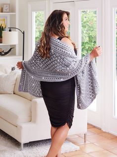 a woman standing in front of a window with a shawl over her shoulders and wearing a black dress