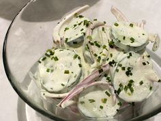 a glass bowl filled with sliced onions covered in white sauce and green onion sprinkles