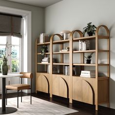 a room with a table, chairs and bookshelf next to a large window