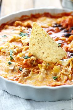 a tortilla chip being dipped with a tortilla chip in a white casserole dish