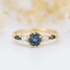 a blue and white diamond ring with three stones on the side, sitting next to some flowers