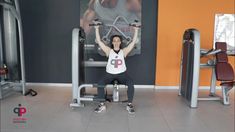 a woman squats on a bench in front of a gym machine with an exercise poster behind her