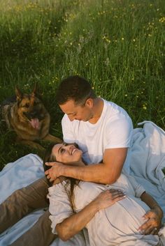 a man and woman laying in the grass next to a dog on a blanket with their eyes closed