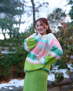 a woman in a green skirt and pink sweater posing for the camera with her hands on her hips