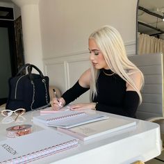 a woman sitting at a table writing on a notebook and holding a pen in her hand