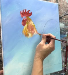 a person is painting a rooster on a piece of paper with watercolor pencils