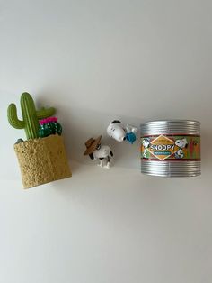 some toys are sitting next to a can of peanuts and a cacti on the wall