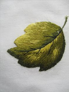 a green leaf is embroidered onto a white fabric piece with gold thread on the edge