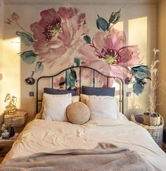 a bed with white sheets and pink flowers painted on the wall