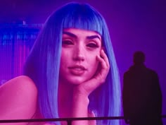 a woman with bright blue hair and purple eyes is looking at a man in a dark room