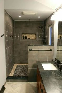 a bathroom with gray tiled walls and black counter tops, along with a walk in shower