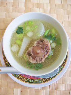 a bowl of soup with meat and vegetables in it on top of a woven place mat