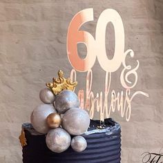 a black cake with silver and gold decorations on it's top is sitting in front of a wall