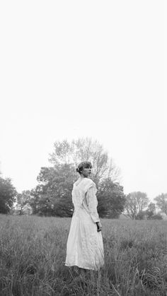 an old photo of a woman standing in the middle of a field with tall grass