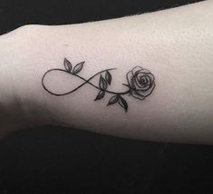 a black and white rose tattoo on the left inner arm, with an infinite symbol