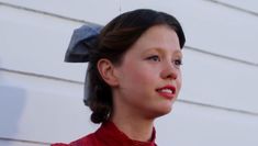 a woman wearing a red dress and a bow on her head is standing in front of a white wall