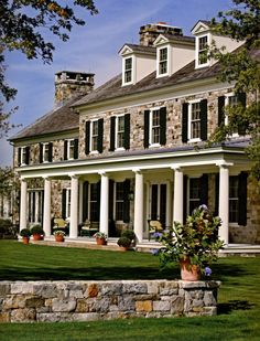 a large stone house with columns on the front and side walls, surrounded by lush green grass