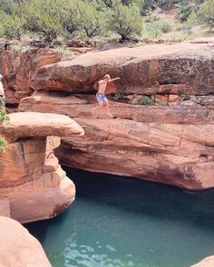 a man standing on top of a cliff next to a body of water in a canyon