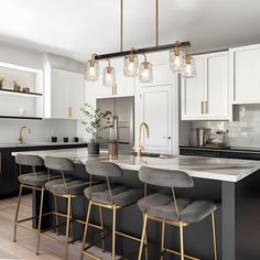 a large kitchen with white cabinets and black counter tops, gold bar stools and pendant lights