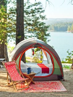 a tent is set up in the woods with a table and chair next to it