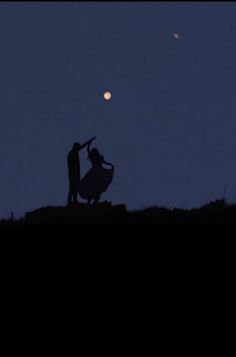 two people standing on top of a hill at night with the moon in the background