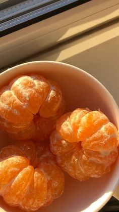 four peeled oranges in a white bowl on a window sill