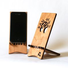 two cell phones stand next to each other in front of a phone holder that has a tree on it