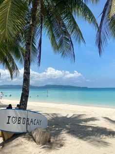 a white surfboard sitting on top of a sandy beach next to the ocean and palm trees