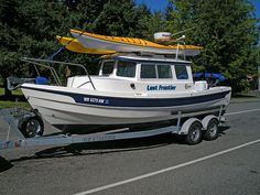 a white boat with a yellow kayak on it's roof is being towed by a trailer