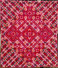 a red and pink quilt is hanging on the wall