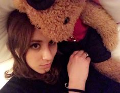 a woman laying in bed with a teddy bear on top of her head and another stuffed animal behind her