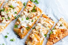 several slices of pizza with various toppings on top of white parchment paper, cut into squares