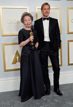 two people standing next to each other in front of an oscars red carpet with one person holding an award