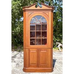 a tall wooden cabinet with glass doors on the top and bottom half, in front of some trees