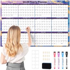 a woman writing on a wall calendar with markers and pencils next to it, along with other office supplies