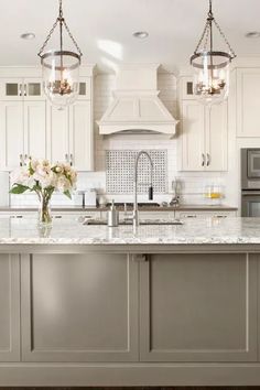 a large kitchen with white cabinets and marble counter tops, two pendant lights over the island