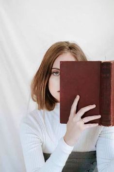 a woman is holding an old book in her hands and looking at the camera while wearing a white sweater