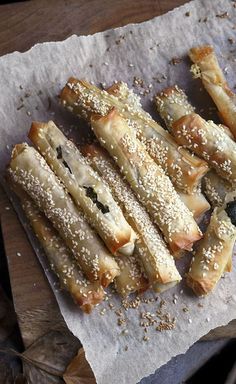 breadsticks with sesame seeds and other toppings on top of parchment paper sitting on a wooden table