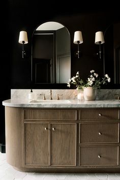 a bathroom vanity with two sinks and three mirrors on it's sides, in front of a black wall