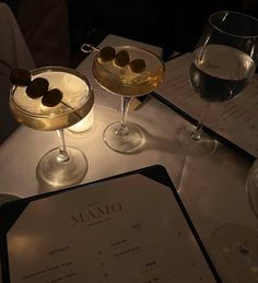 two martinis with olives sit on a table next to a menu and wine glasses