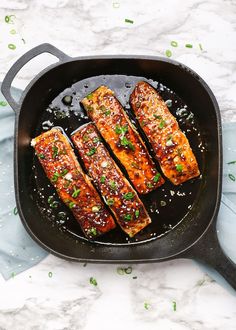 salmon fillets in a cast iron skillet with green onions and seasoning on the side