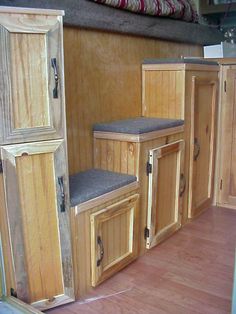 the inside of a camper with wooden cabinets and gray cushioned seat covers on it