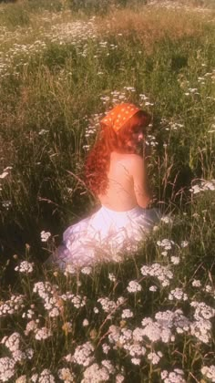 a woman with red hair is sitting in the middle of a field full of flowers