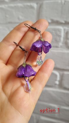 a person holding some kind of purple flower in their hand and wearing it as a clip on earring