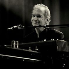 a man sitting at a keyboard with a microphone in front of him and looking to the side